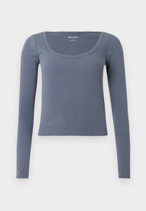 Top cu mâneci lungi, cu model reiat, în culoarea albastru ardezie, cu decolteu rotund și design mulat. Confecționat dintr-un amestec moale și elastic de bumbac.