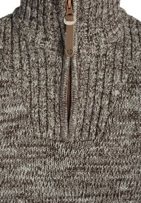 Brown and cream knitted sweater with a high collar, half-zipper, and textured pattern. Features a contrasting zipper accent.