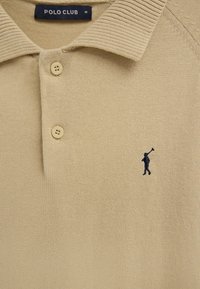 Beige Poloshirt mit zwei Knöpfen, geripptem Kragen, navyblau gesticktem Polo-Spieler-Logo und "POLO CLUB" Größenetikett M innen.