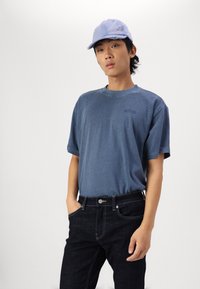 Blue cotton t-shirt with short sleeves, round neck, and small logo; paired with dark denim jeans featuring standard pockets and stitching.