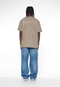 Maslinasto zelena prevelika majica s bijelim natpisom "YOUTH" na leđima, u kombinaciji s svijetlosmeškim, iznošenim širokim trapericama.