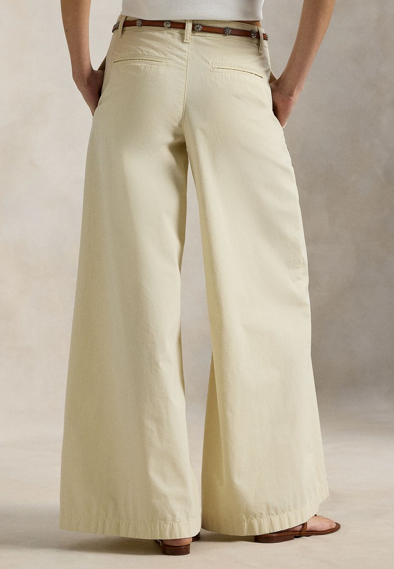 Pantalon à jambes larges en tissu doux de couleur jaune clair, présentant une texture lisse, deux poches arrière et un ourlet avec un revers subtil.