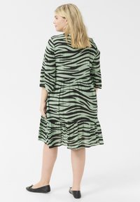Grön klänning med svarta zebra-ränder, trekvartsärmar, lager-på-lager fåll och en avslappnad passform. Matchad med svarta flats.