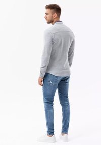 Grijze longsleeve polo met een geribbelde kraag en subtiele strepen, gecombineerd met versleten blauwe jeans en witte sneakers.