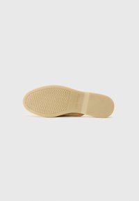 Tan shoe sole with a textured rubber surface. Features a wavy pattern for traction and embossed branding. Smooth finish with a neutral color.