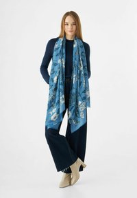 Blauwe sjaal met een bloemenpatroon, gemaakt van lichtgewicht materiaal, weergegeven bovenop een donkere outfit, die elegant valt.