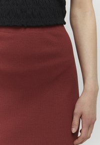 Gerüschter, roter Rock aus dehnbarem Stoff mit tailliertem Design. Der Bund zeigt geraffte Details, während eine glatte Oberfläche sichtbar ist.