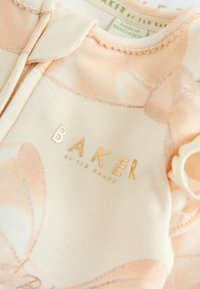 Gai persiku kokvilnas apģērbs ar ziedu rakstu, ar zelta "BAKER" logotipu, mīksta tekstūra un viļņotām malām apkakles pusē.