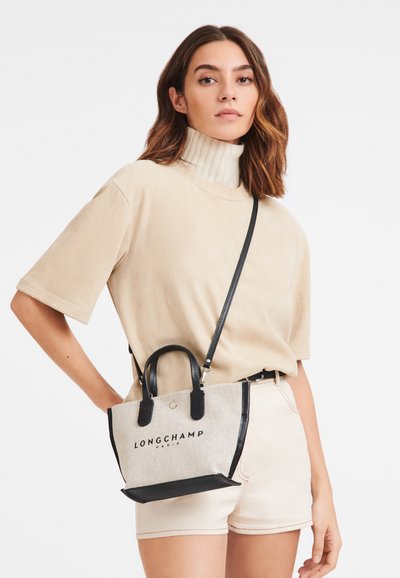 Graue Canvas-Handtasche mit schwarzen Lederakzenten, ausgestattet mit doppelten Griffen und einem abnehmbaren Riemen, der "LONGCHAMP PARIS" in schwarzem Text zeigt.