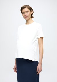 Biała koszulka ciążowa z krótkimi rękawami, okrągłym dekoltem i luźnym krojem. Do niej granatowa spódnica. Gładka faktura tkaniny.