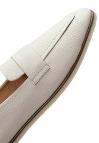 Mocassin en cuir blanc texturé avec une semelle plate et une large lanière traversant la partie supérieure de la chaussure.