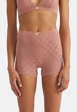 Woman wearing matching dusty pink Adidas sports bra and high-waisted shorts with embossed trefoil pattern and logo on waistband.