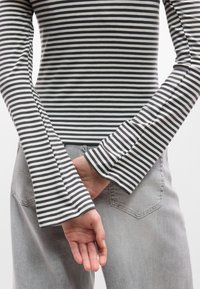 Μπλούζα μακρυμάνικη με μαύρες και λευκές ρίγες και φαρδιές μανσέτες, συνδυασμένη με ανοιχτό γκρι τζι ν, που αναδεικνύει το απαλό ύφασμα και το εφαρμοστό σχέδιο.