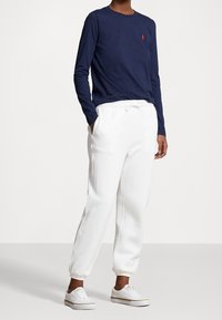 Mörkblå långärmad skjorta med en liten röd logotyp, i kombination med vita joggers med elastisk midja och vita sneakers, med dragsko-detalj.