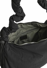 Sort stof skuldertaske med en skrumpet håndtag, lynlåslukning og et olivengrønt interiør med en lille lynlåslyne.