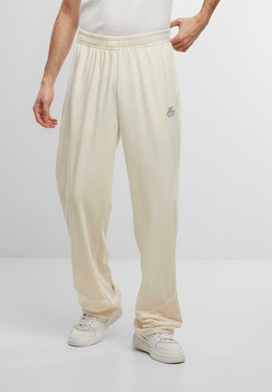 Cream-colored, loose-fit sweatpants made of soft fabric with an elastic waistband. Features a small logo detail on the left thigh.