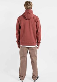 Sweat à capuche bordeaux et pantalon beige, avec une coupe décontractée. Le tissu semble doux, avec une poche kangourou et des poignets côtelés.