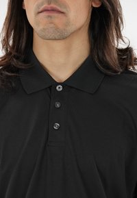 Sort polo shirt med en klassisk krave og tre-knap lukning, lavet af et struktureret stof med en glat overflade.