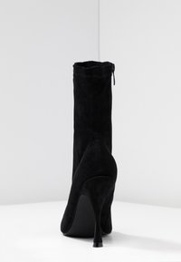 Svart mocka ankelboot med hög stilettklack. Har en texturerad yta och en dragkedja bak. Ren, minimalistisk design.