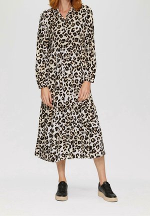 Kvinde iført en langærmet, knappet leopardprintkjole med en flæset nederdel, kombineret med sorte plateau-sneakers.