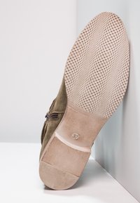 Bottine en daim kaki avec une semelle en caoutchouc texturée, dotée d'une fermeture éclair latérale et d'un talon rond et plat. Taille indiquée sur la semelle.