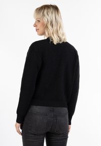 Pulover negru tricotat cu un design scurt, textură cu dungi și mâneci lungi. Asortat cu blugi închiși la culoare, văzut din spate.