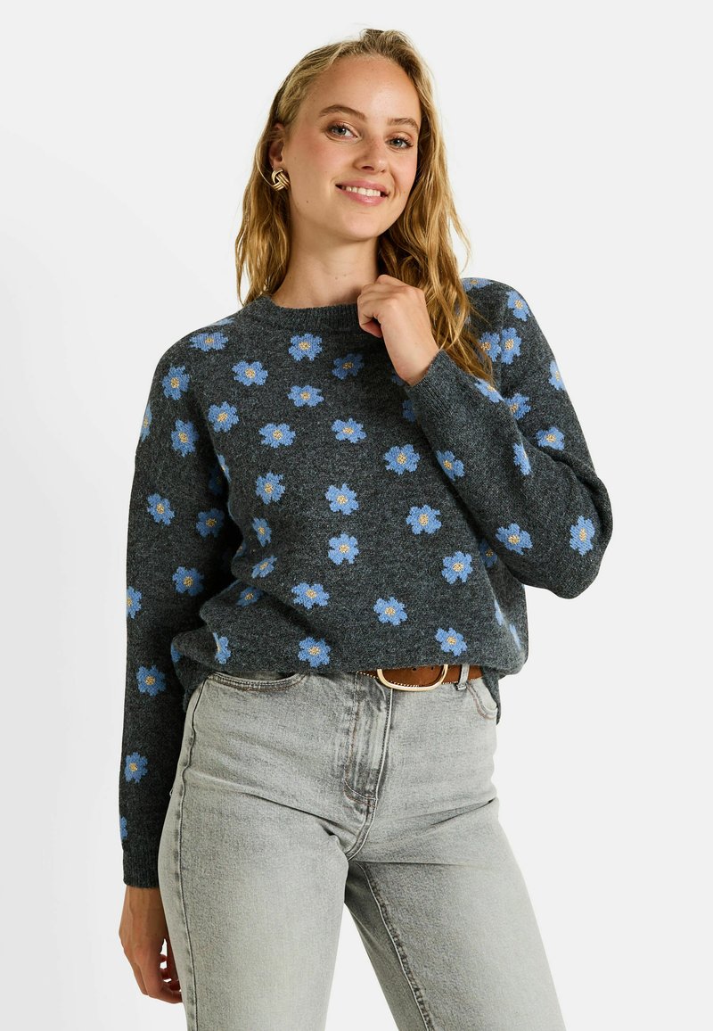 Pull gris avec un motif floral bleu clair, col rond et manches longues. Associé à un jean gris clair et une ceinture marron. Texture douce.
