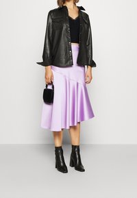 Czarna skórzana koszula zapinana na guziki, czarny koronkowy top w stylu cropped, jasnofioletowa satynowa spódnica w kształcie dzwonu oraz czarne botki na obcasie, zestawione z małą czarną torebką.