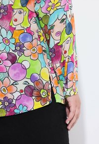 Blusa colorata con un motivo floreale e facciale, caratterizzata da colori vivaci come il rosa, il blu, il giallo e il verde. Realizzata in tessuto leggero.