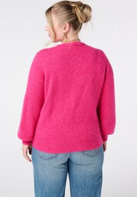 Zachte roze trui met lange, licht opgeblazen mouwen en geribbelde zoom; gecombineerd met lichtblauwe jeans die een casual pasvorm laten zien.