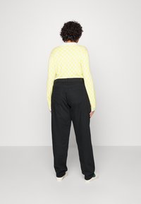 Geel gebloemd sweater met lange mouwen en zwarte wijde broek, die een ontspannen pasvorm en minimale details toont.