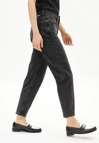 Jean en denim noir taille haute, jambes fuselées et poches avant, associé à des mocassins noirs ornés d'accents blancs sur le dessus.