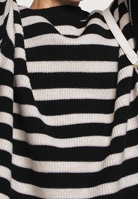 Czarny i kremowy sweter dzianinowy w paski z prążkowanym dekoltem. Miękka tekstura, luźny krój, z naprzemiennie szerokimi paskami.