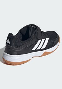 Čierna atletická topánka s vrchnou časťou z messu, biely trojprúžok, nastaviteľný popruh, polstrovaný golier a gumová podrážka pre trakciu.