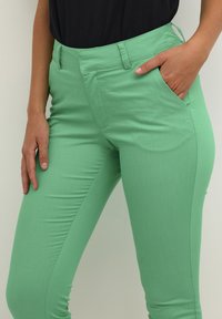Green stretch pants with a slim fit, featuring front pockets, a smooth texture, and a classic waistband design.