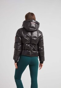 Chaqueta de plumas negra con un acabado brillante, capucha ajustada y patrón acolchado. Cuenta con puños elásticos y una etiqueta con el logotipo rosa en el cuello.