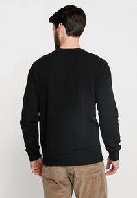 Svart sweatshirt med långa ärmar, rund halsringning och ribbad avslutning. Slät textur, figurnära design med sömdetaljer på axlarna.