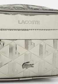 Borsa Lacoste nella trama geometrica argento con logo embossato, dotata di un piccolo accento a forma di coccodrillo e una finitura liscia e lucida.