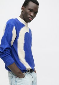 Suéter de punto a rayas azules y crema con cuello redondo acanalado y mangas largas, combinado con jeans de mezclilla azul claro.