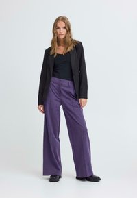 Blazer noir ajusté, haut noir moulant et pantalon large violet. Tissu texturé avec une finition lisse et des coutures discrètes. Chaussures noires.