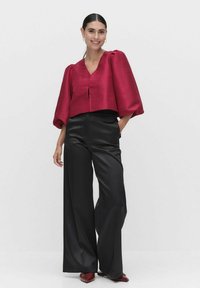 Skåret, dyb rød satinbluse med pufærmer, parret med høj talje, sorte brede bukser. Løs pasform, minimal detaljering, elegant design.