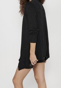 Svart stickad tröja med en lös passform, ribbade ärmslut och flerfärgade prickar överallt. Avslutningen är längre på baksidan, vilket ger en avslappnad silhuett.