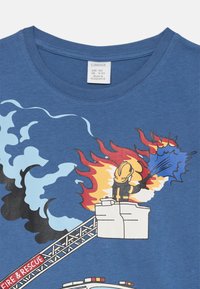 Blaues T-Shirt aus Baumwolle mit Rundhalsausschnitt. Mit einem Grafik eines Feuerwehrmanns, der mit einem Schlauch gegen Flammen und Rauch kämpft.