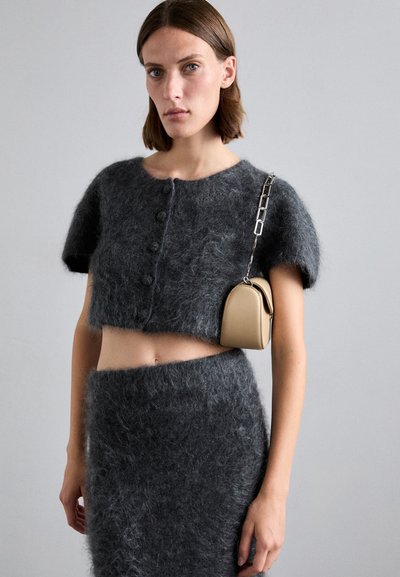 Top corto in misto mohair grigio con maniche corte, caratterizzato da bottoni circolari. Abbinato a una gonna pelosa coordinata e una piccola borsa beige.