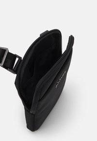 Pochette in tessuto nero con chiusura a zip, caratterizzata da una superficie testurizzata e tasche interne. Cinghia regolabile attaccata.