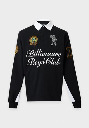 Jeune homme debout portant un polo noir à manches longues avec col blanc, patchs logo, texte "Billionaire Boys Club", jean large foncé et chaussures noires et blanches.
