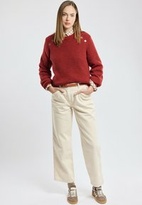 Pull rouge côtelé avec boutons décoratifs, pantalon large crème, et baskets marron avec des rayures blanches. Superposé avec une chemise à carreaux.