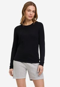 Haut à manches longues noir fabriqué en tissu doux, associé à un short gris clair texturé présentant des motifs verticaux et une coupe décontractée.