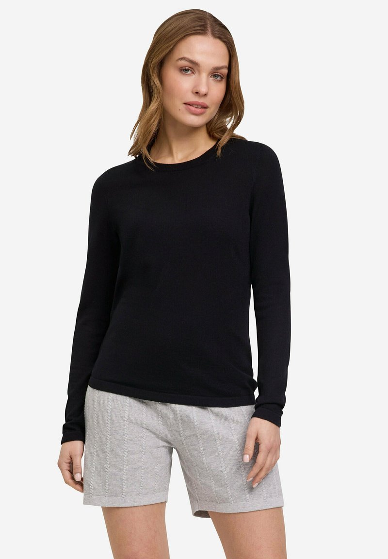 Haut à manches longues noir fabriqué en tissu doux, associé à un short gris clair texturé présentant des motifs verticaux et une coupe décontractée.