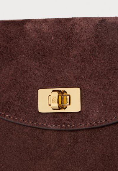 Gros plan sur un sac en daim marron avec une fermeture à loquet tournant rectangulaire dorée sur le rabat.